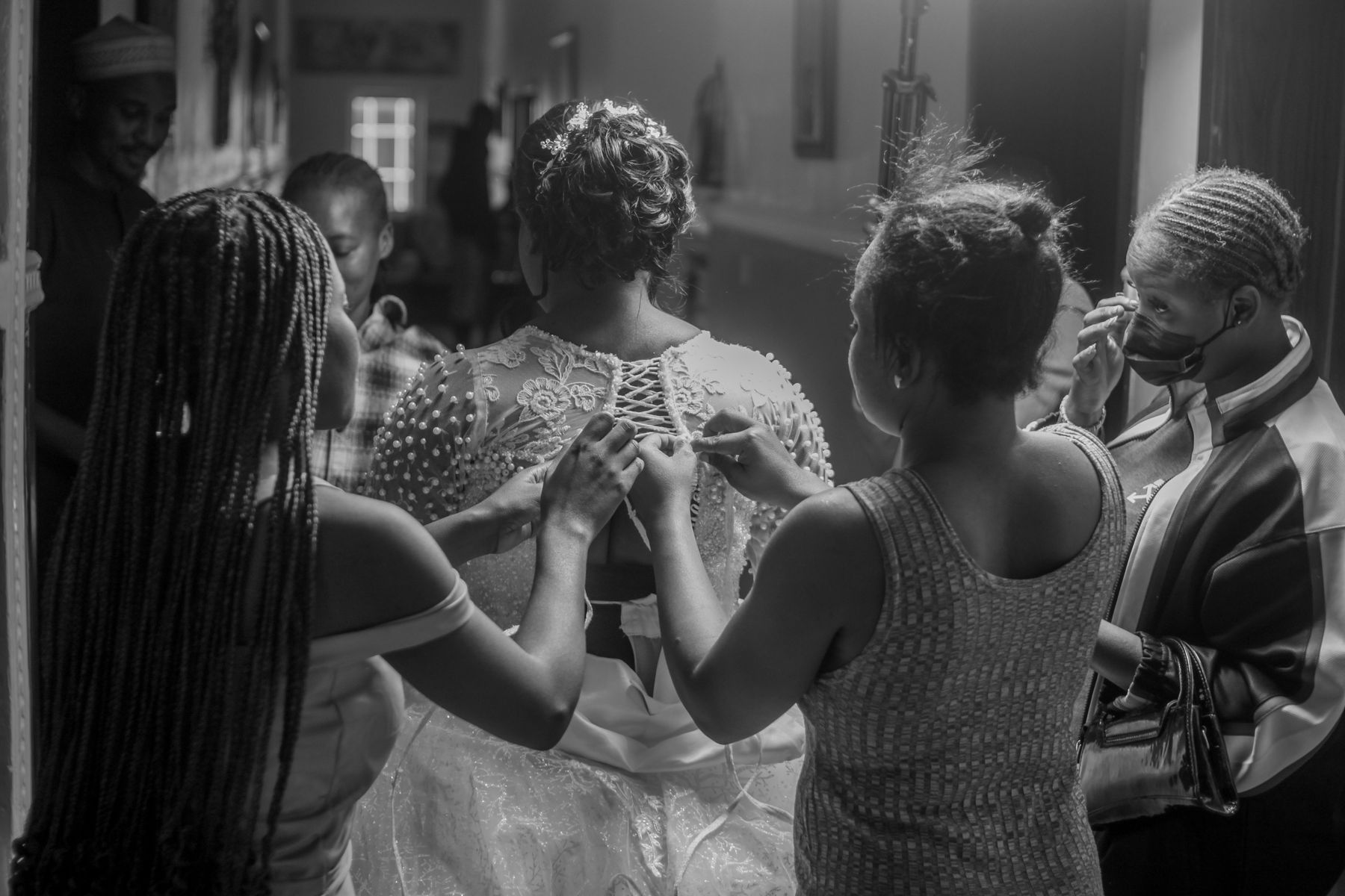 Bridesmaids helping a bride get ready in a candid black-and-white photograph