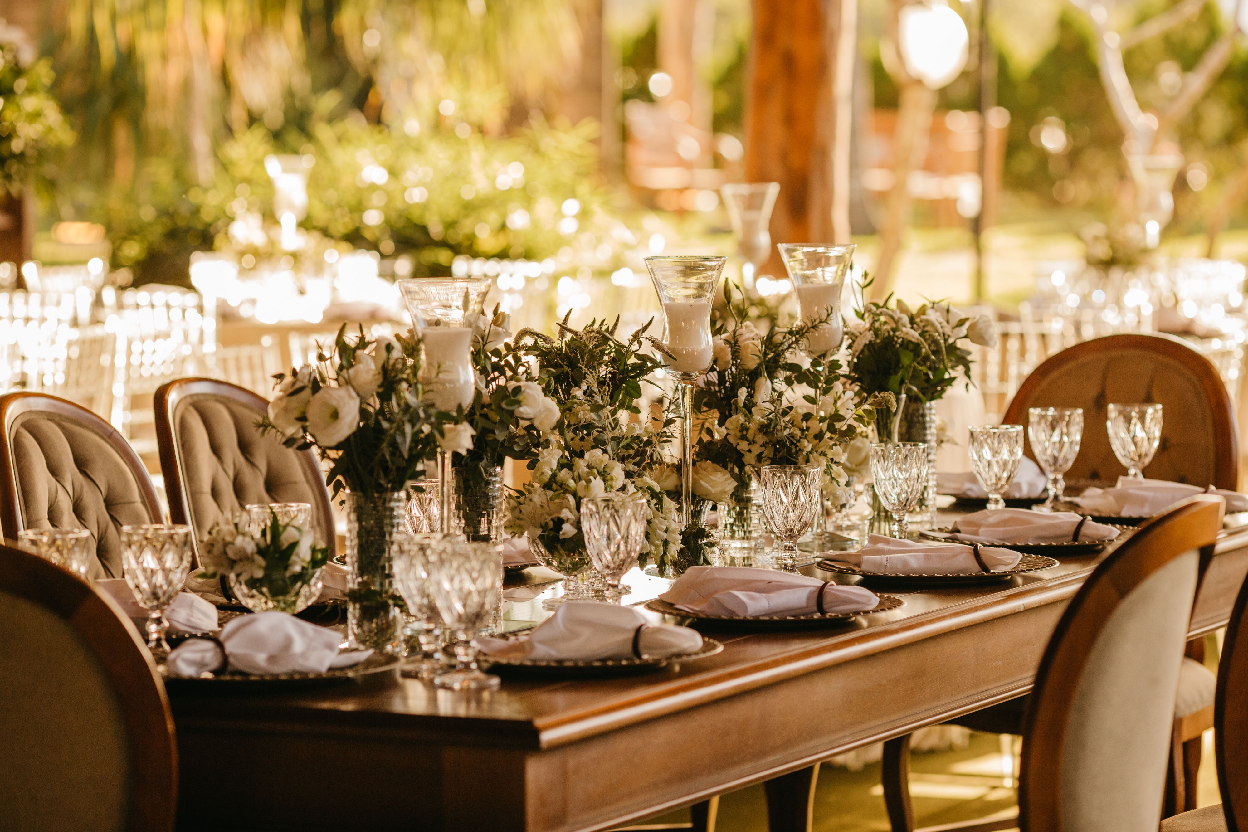 Long wedding reception table arranged outdoors beneath trees